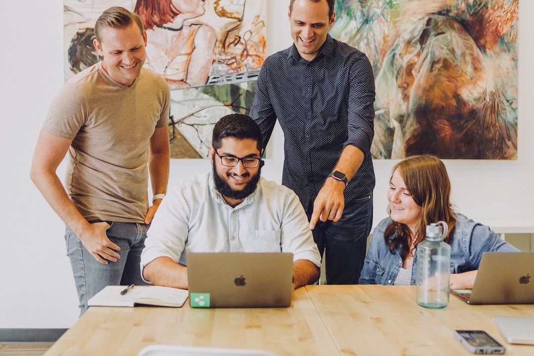Four people smiling and looking at a laptop after choosing an easy proposal automation solution.